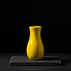 Bright yellow vase on a dark stone surface with a black studio background