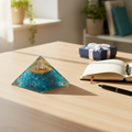 Turquoise Firoza crystal pyramid displayed on a meditation or home-office table beside a notebook and gift box