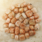 Polished Sunstone tumble stones arranged on a warm natural stone surface