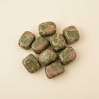 Polished Unakite tumble stones arranged on an ivory studio background