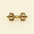 Front view of an ornate gold-tone Vajra Dorje on a warm ivory background