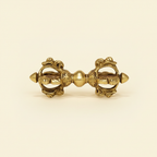 Front view of an ornate gold-tone Vajra Dorje on a warm ivory background