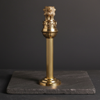 Tall brass Ashoka Pillar-inspired decor displayed on dark natural stone