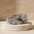 Layered silvery muscovite chips displayed on a light stone pedestal
