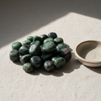 Polished Ruby Zoisite tumble stones arranged on a neutral linen surface