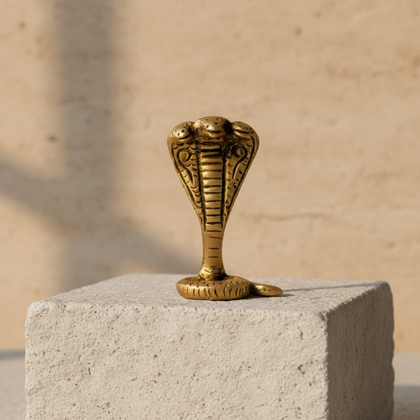 Gold-brass cobra snake figurine displayed on a light stone pedestal