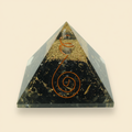 Natural 7 Chakra crystal pyramid with dark crystal tones and gold-toned inclusions on an ivory background