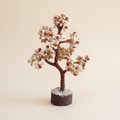 Rudraksha Gomti Chakra tree with pale stones, red accents, reddish-brown branches, and dark wood base on an ivory background