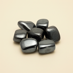 Polished hematite tumble stones arranged on a warm ivory background
