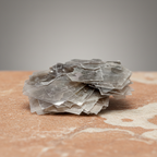 Layered silvery muscovite chips on a warm terracotta and cream stone surface