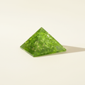 Front view of a bright green Peridot crystal pyramid on a warm white background