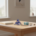 Blue-and-white Evil Eye protection pyramid displayed on an entryway or home-office table beside a notebook and gift box