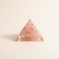 Front view of a soft pink Rose Quartz crystal pyramid on a warm white background