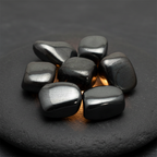 Polished hematite tumble stones arranged on a charcoal stone surface