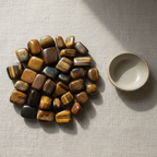 Polished Tiger's Eye tumble stones arranged on a neutral linen surface